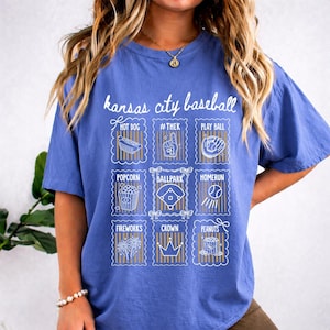 May include: A blue t-shirt with the words "Kansas City Baseball" in white script. Below the text are nine white and gold illustrations of baseball-related items, including a hot dog, popcorn, and a baseball.