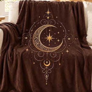 May include: A dark brown plush throw blanket featuring a large, intricate gold-colored graphic of a crescent moon surrounded by swirling filigree patterns, small stars, and a central four-pointed star, centered on the fabric surface.