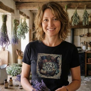 May include: A black t-shirt featuring a patriotic design with an American flag, a witch's hat, and the text "July 4 1776." The design is printed on a black t-shirt.