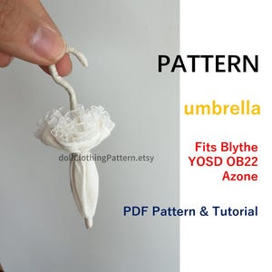 May include: A miniature off-white umbrella with a ruffled canopy and a curved handle. The text reads: PATTERN umbrella Fits Blythe YOSD OB22 Azone PDF Pattern & Tutorial. The umbrella is held by a finger, showcasing its small scale for dolls.