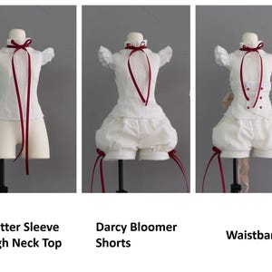 Puede incluir: Un top blanco de cuello alto con mangas de volantes y una cinta roja, bombachos blancos con lazos de cinta roja y una banda blanca con botones rojos.