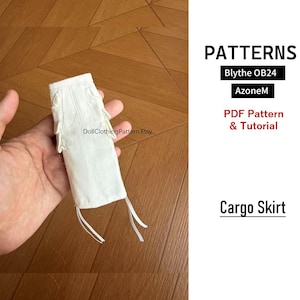 May include: A white doll cargo skirt with side pockets and dangling fabric ties. The text on the image reads PATTERNS, Blythe OB24, AzoneM, PDF Pattern & Tutorial, DollClothingPattern.Etsy, and Cargo Skirt. The skirt is shown in a hand.