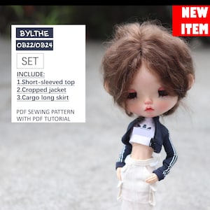 May include: A doll wearing a white short-sleeved top, a navy blue cropped jacket with white stripes, and a white cargo skirt. The doll has brown hair and is wearing a white headband. The doll is a Blythe doll, a type of fashion doll. The image includes the text "BYLTHE OB22/OB24 SET INCLUDE: 1.Short-sleeved top 2.Cropped jacket 3.Cargo long skirt PDF SEWING PATTERN WITH PDF TUTORIAL NEW ITEM".