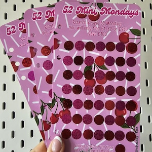 May include: Three pink rectangular savings tracker cards with a cherry pattern and white sprinkles. The text reads 52 Mini Mondays, Scratch & save 52 Mondays. You will only find £1, £2 or £3s! Save £100, and A bonus scratch off for those years that have 53 Mondays.
