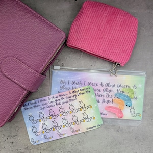 May include: A selection of stationery items in pink and purple. Features a leather-look planner, a corduroy zipped pouch, and two clear pouches with worm illustrations and the text "Oh I wish I were a glow worm..."