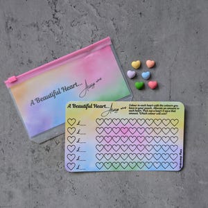 May include: A clear plastic pouch and a savings tracker card with a rainbow watercolour design. The pouch and card both have the text "A Beautiful Heart... Always wins". Several heart-shaped sweets are scattered around.