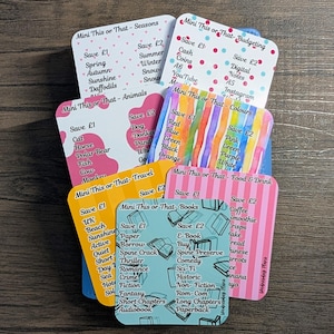 May include: A stack of square cards with different themes, including seasons, animals, and travel. Each card has a list of items and the text "Mini This or That". The cards are in various colors, with some text visible on each card.
