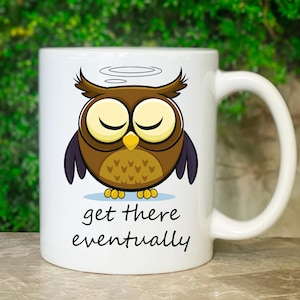 Könnte beinhalten: Weiße Keramik-Tasse mit einem Cartoon-Eulen-Design. Die Eule hat braune Federn, einen gelben Schnabel und geschlossene Augen. Auf der Tasse steht der Text "get there eventually" in schwarzer, handschriftlicher Schrift. Die Eule hat einen Heiligenschein über ihrem Kopf.