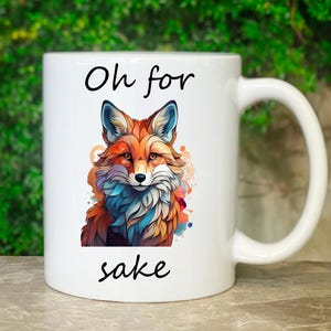 Könnte beinhalten: Weiße Keramik-Kaffeetasse mit einer bunten Fuchsillustration und dem Text "Oh for sake" darauf.