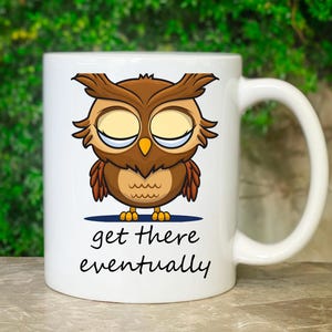 Könnte beinhalten: Weiße Keramik-Kaffeetasse mit einer Cartoon-Eule mit geschlossenen Augen und dem Text "get there eventually".