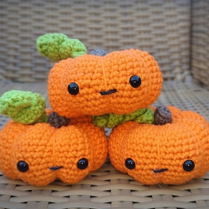 May include: Three crocheted orange pumpkins with green stems and black eyes. The pumpkins are stacked on top of each other.