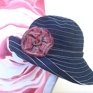 May include: A navy blue and white striped sun hat with a large red and white plaid flower accent.