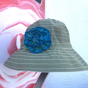 Puede incluir: Un sombrero de sol a rayas verde y blanco con una gran flor de tela azul y verde.