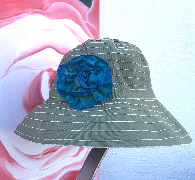 Puede incluir: Un sombrero de sol a rayas verde y blanco con una gran flor de tela azul y verde.