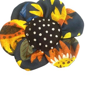 May include: A blue fabric flower with yellow and orange sunflower patterns. The center of the flower is black with white polka dots.