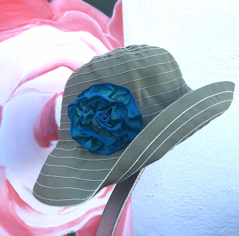 Puede incluir: Un sombrero de sol verde con un ala ancha y un adorno de flor de tela azul.