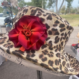 May include: A brown and tan leopard print sun hat with a large red and orange fabric flower on the top.