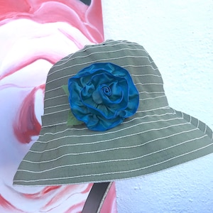 Puede incluir: Un sombrero de sol a rayas verde y blanco con una gran flor de tela azul.