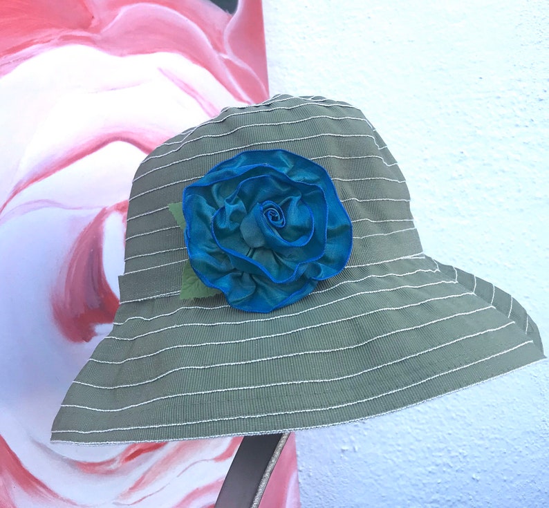 Puede incluir: Un sombrero de sol a rayas verde y blanco con una gran flor de tela azul.