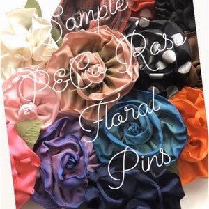 Puede incluir: Una colecci&oacute;n de pinzas para el pelo de flores de tela en varios colores y patrones, incluyendo rojo, blanco, negro, azul, verde y marr&oacute;n. Las flores est&aacute;n dispuestas en forma de ramo y tienen un dise&ntilde;o en capas y con volantes. El texto "Sample Rose P&Co Floral Pins" est&aacute; escrito en la imagen.