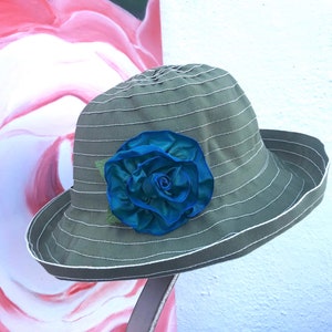 Puede incluir: Un sombrero de sol a rayas verde y blanco con una gran flor de tela azul.