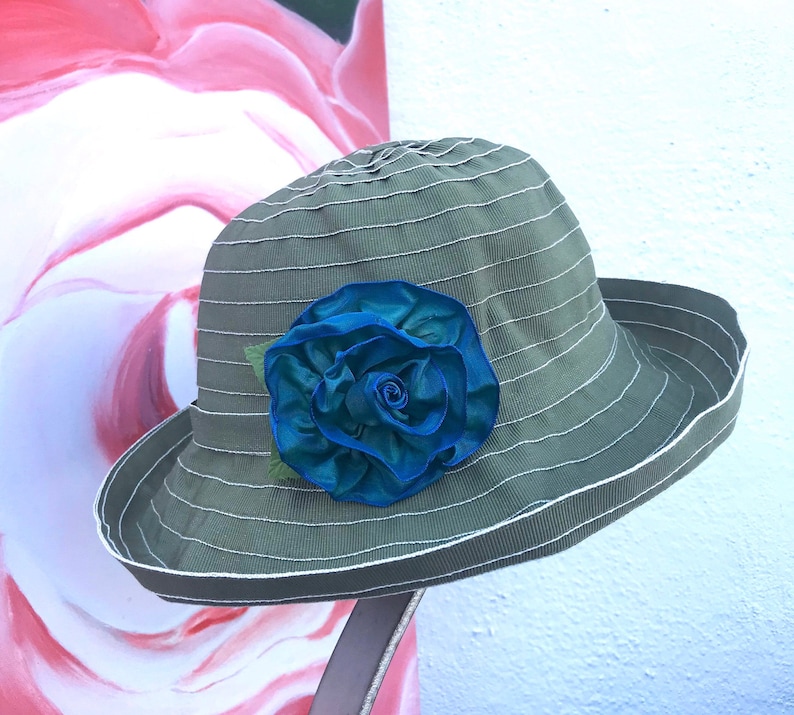 Puede incluir: Un sombrero de sol a rayas verde y blanco con una gran flor de tela azul.