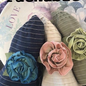 Puede incluir: Tres sombreros de sol plegables con rosetas de tela de diferentes colores. Los sombreros son a rayas y tienen un ala ancha. Las rosetas son en tonos de rosa, verde y azul.