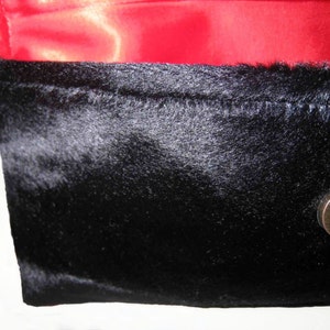 May include: A black faux fur clutch with a red satin lining and a brass clasp.