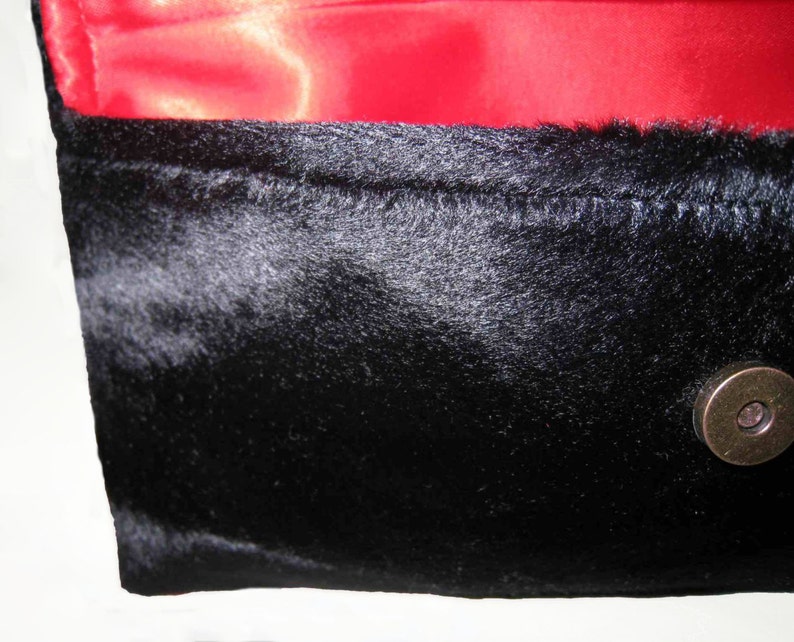 May include: A black faux fur clutch with a red satin lining and a brass clasp.