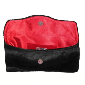 May include: Black velvet clutch with a red satin lining and a snap closure. The clutch has a small pocket on the inside.