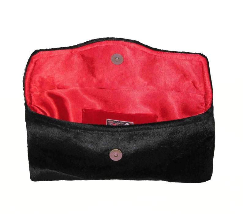 May include: Black velvet clutch with a red satin lining and a snap closure. The clutch has a small pocket on the inside.