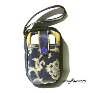 May include: A small blue and gold patterned fabric phone case with a blue button closure and a black strap.