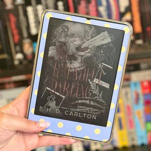 May include: A digital e-reader featuring a light blue protective case with yellow polka dots. The screen displays the book cover for "Dreadful Darling" by H. D. Carlton, which features a skull, keys, and wings in a dark, gothic-inspired illustration.