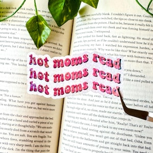 May include: A pink and white sticker with the text "hot moms read" in a retro font. The sticker is slightly wrinkled and has a glittery finish.