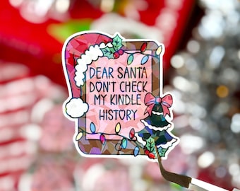 May include: A colorful Christmas sticker with the text "Dear Santa Don't Check My Kindle History." The sticker features a Santa hat, Christmas lights, and a Christmas tree. The sticker is held by tweezers.