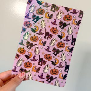 May include: A rectangular sticker sheet with a light purple background featuring a repeating pattern of Halloween icons including orange jack-o'-lanterns, white ghosts, black cats, purple witch hats, orange crescent moons, and small gold stars.
