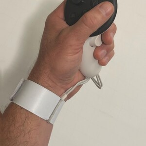 May include: A white wrist strap with a black and white controller attached. The controller has a black button and a white button with a symbol on it.