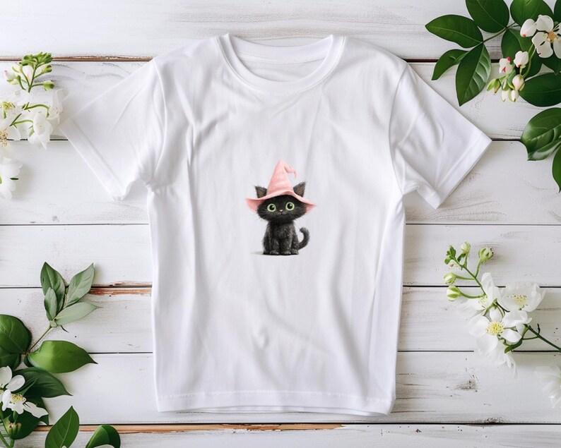 May include: White t-shirt with a black cat illustration wearing a pink witch's hat. The cat has large green eyes. The design is a whimsical illustration, suitable for Halloween or cat enthusiasts.
