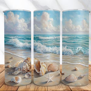 Puede incluir: Tres vasos de acero inoxidable con una escena de playa y conchas marinas. Los vasos muestran un océano azul con olas blancas rompiendo en una playa de arena. La playa está decorada con conchas marinas, incluyendo una gran concha, una estrella de mar y varias conchas más pequeñas.