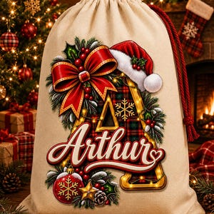 Pode incluir: Um saco de presente bege com cordão, apresentando uma letra A grande com um padrão xadrez vermelho e verde. A letra é decorada com um laço vermelho, um gorro de Pai Natal, azevinho e o nome Arthur em escrita branca. Um enfeite e estrela.