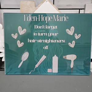 May include: A teal sign with the text "Eden Hope Marie" and "Don't forget to turn your hair straighteners off." The sign features illustrations of a hairbrush, straightener, hair product, and a hairdryer. White hearts are scattered around the text.