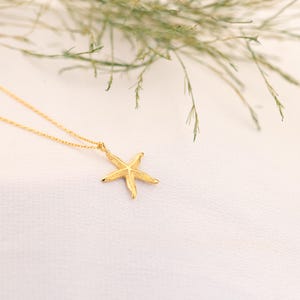 May include: A gold chain necklace with a delicate starfish pendant. The pendant is textured and has a slightly raised design.