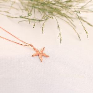 May include: A delicate rose gold necklace featuring a starfish pendant. The starfish is detailed and has a textured finish.