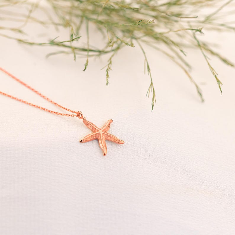 May include: A delicate rose gold necklace featuring a starfish pendant. The starfish is detailed and has a textured finish.