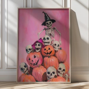 Puede incluir: Impresión enmarcada con temática de Halloween con calabazas talladas y calaveras. Un esqueleto con sombrero de bruja está encima de las calabazas. El fondo es de color rosa. El texto "VIVIDWALLDECOR" está en la esquina superior izquierda.