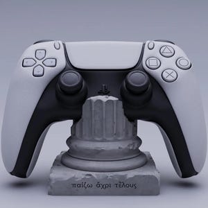 May include: A white and black PlayStation 5 DualSense controller is displayed on a gray stone pedestal with the inscription "παίζω άχρι τέλους" in Greek.