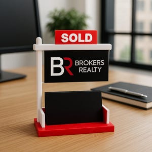 May include: A miniature white and red real estate sign holder featuring a black rectangular sign with the white and red text BROKERS REALTY and a BR logo. A red rectangular topper displays the white text SOLD above the main sign.