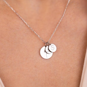 Peut inclure: Un collier en chaîne argent avec trois petits disques argentés en pendentifs. Les disques sont gravés de lettres.