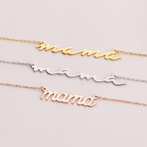 以下が含まれることがあります： それぞれに「mama」という単語が筆記体で書かれた3つの金のネックレス。ネックレスは重ねてあり、一番上に金のネックレス、その下に銀のネックレス、そして一番下にローズゴールドのネックレスが重ねられています。