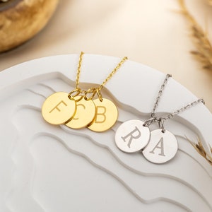 May include: Two necklaces with personalized initial charms. The first necklace has three gold charms with the letters F, C, and B. The second necklace has two silver charms with the letters R and A.